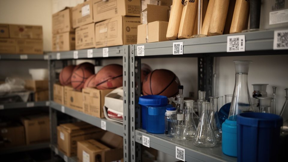 Illustration: a school store room with labelled cartons, sports equipment and lab glassware on metal shelves